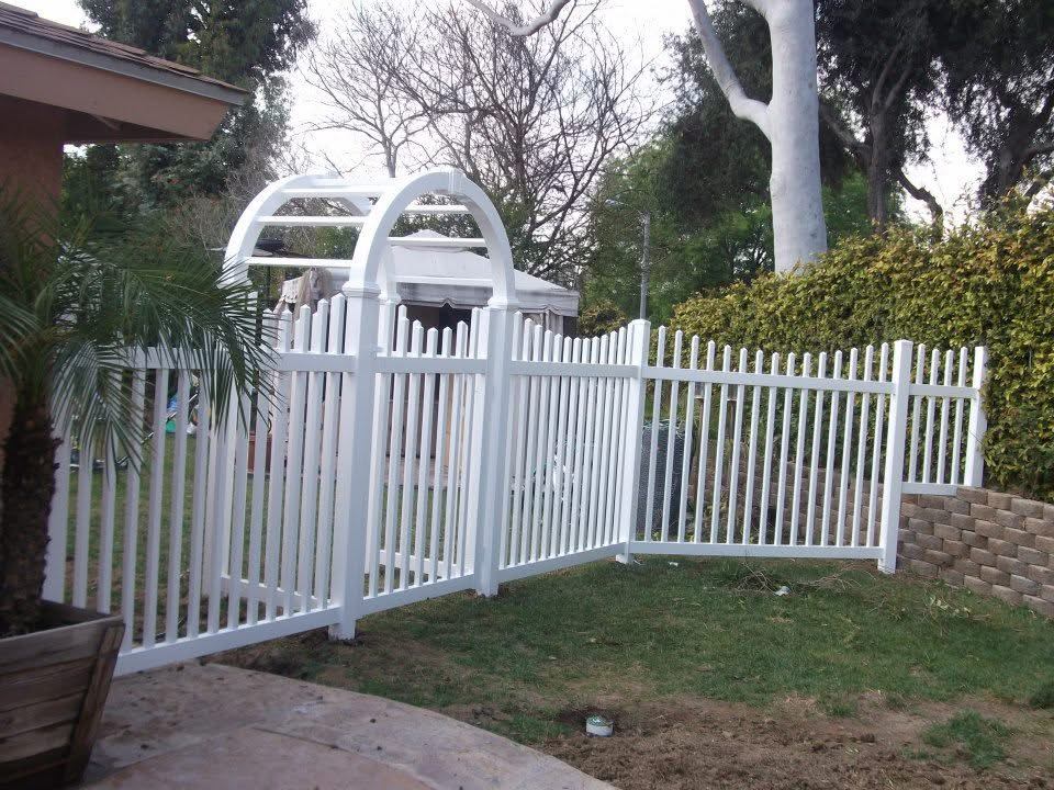 White vinyl picket fence with arched arbor gate around a backyard pool